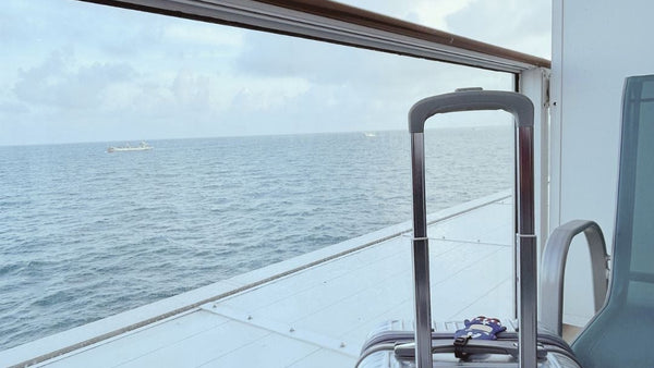 Silver hard-shell suitcase on a cruise ship balcony overlooking the ocean, ideal for travel gift inspiration